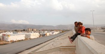 Syrian refugee children sit on a wall overlooking an 'informal tented settlement' in Lebanon's Bekaa valley. The mountains in the background form the border with Syria. Source: Russell Watkins/Department for International Development https://bit.ly/3bLatIm