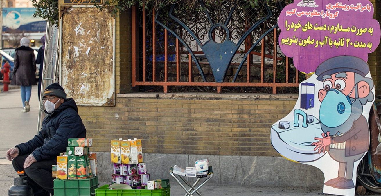 A man wearing a mask selling juice on the street next to a sign encouraging hand washing in the city of Arak in Iran.  Source: Mohsen Malek Hosseini https://bit.ly/2WsKy3p