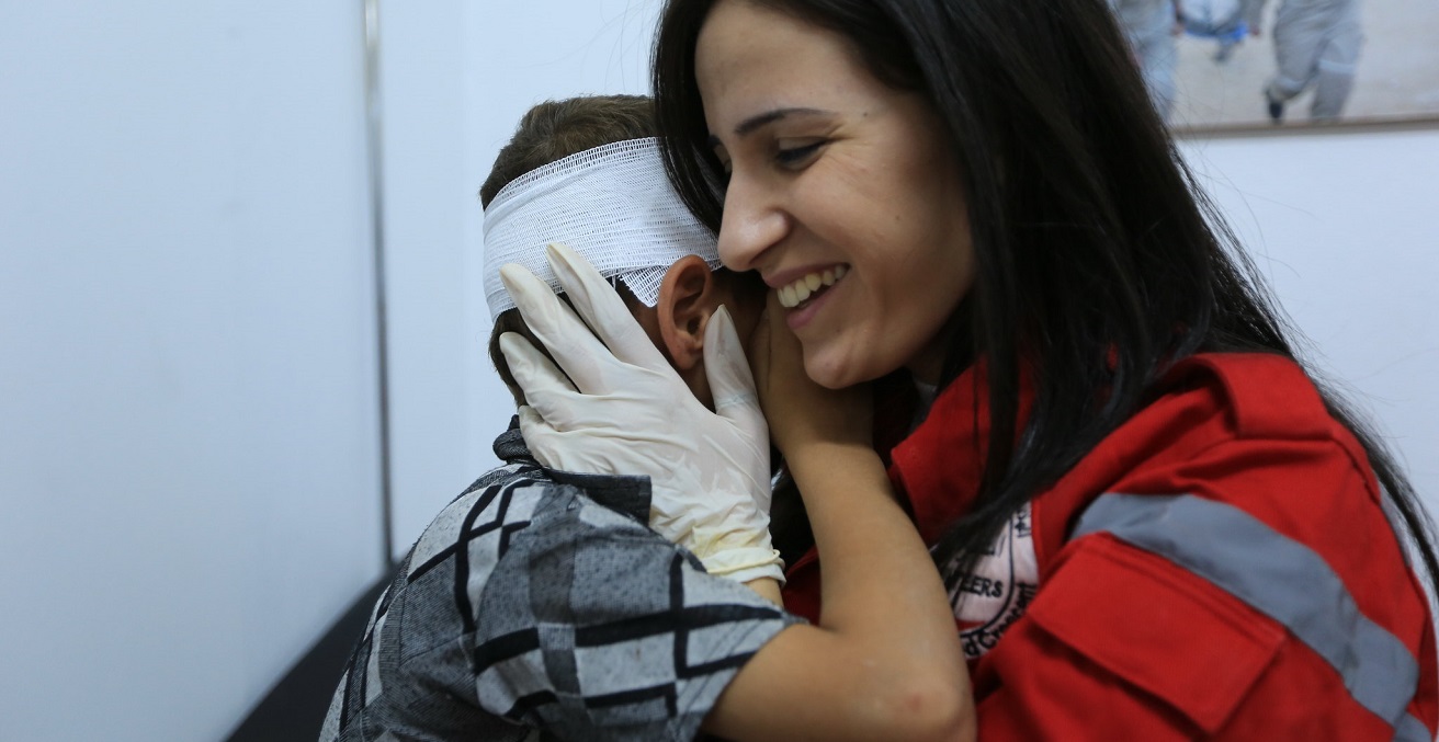 A Syrian Arab Red Crescent volunteer holds a boy after treating his injures. Source:  ICRC/Ibrahim Malla https://bit.ly/2SDP6oy