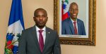 Claude Joseph stands next to a portrait of assassinated president  Jovenel Moise. Source: Rency Inson Michel https://bit.ly/3yaTjA0