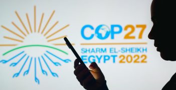 In this photo illustration, a woman's silhouette holds a smartphone with the 2022 United Nations Climate Change Conference COP27 logo in the background. Source: rafapress/Shutterstock.